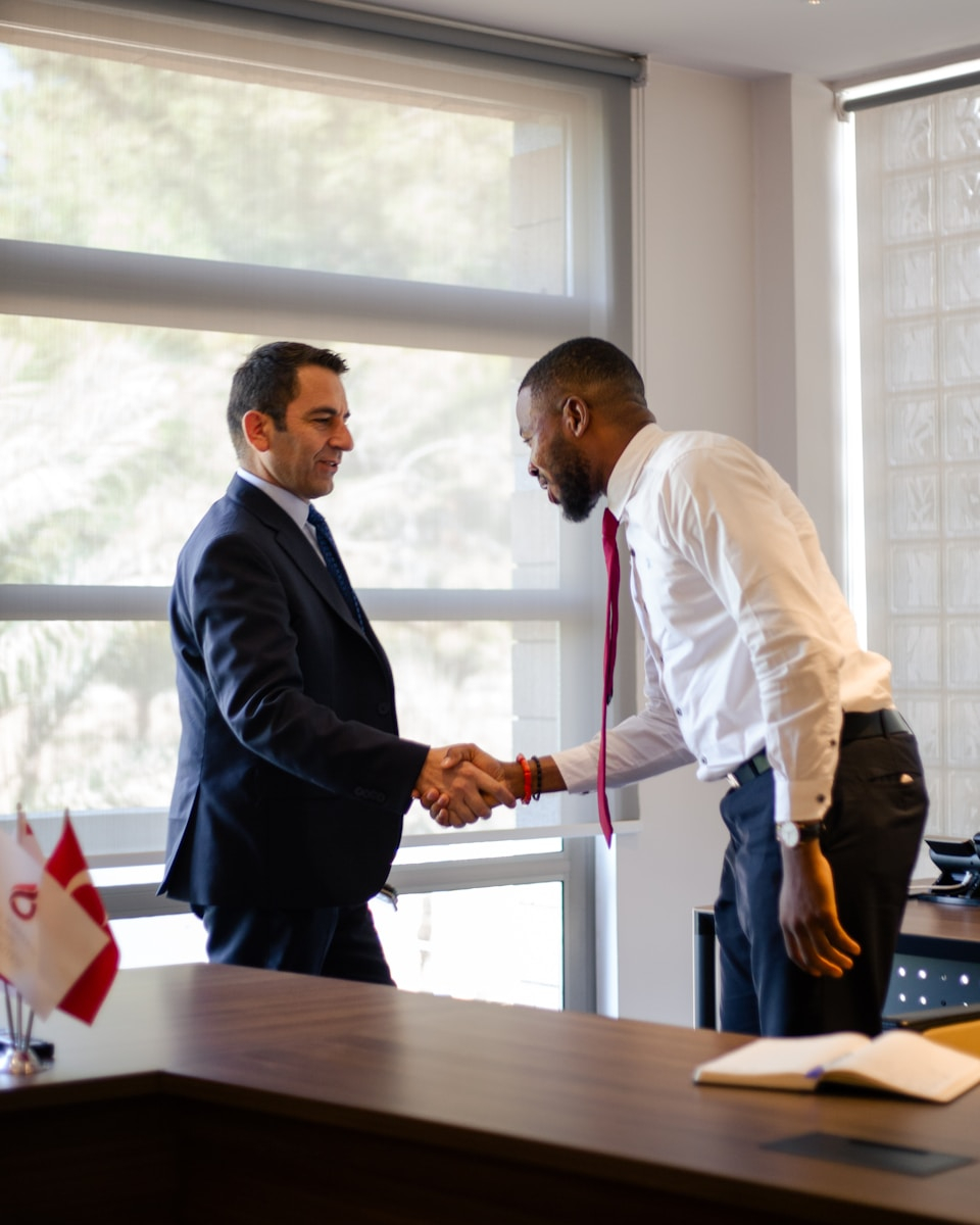 Two businessmen shaking hands across a desk.
